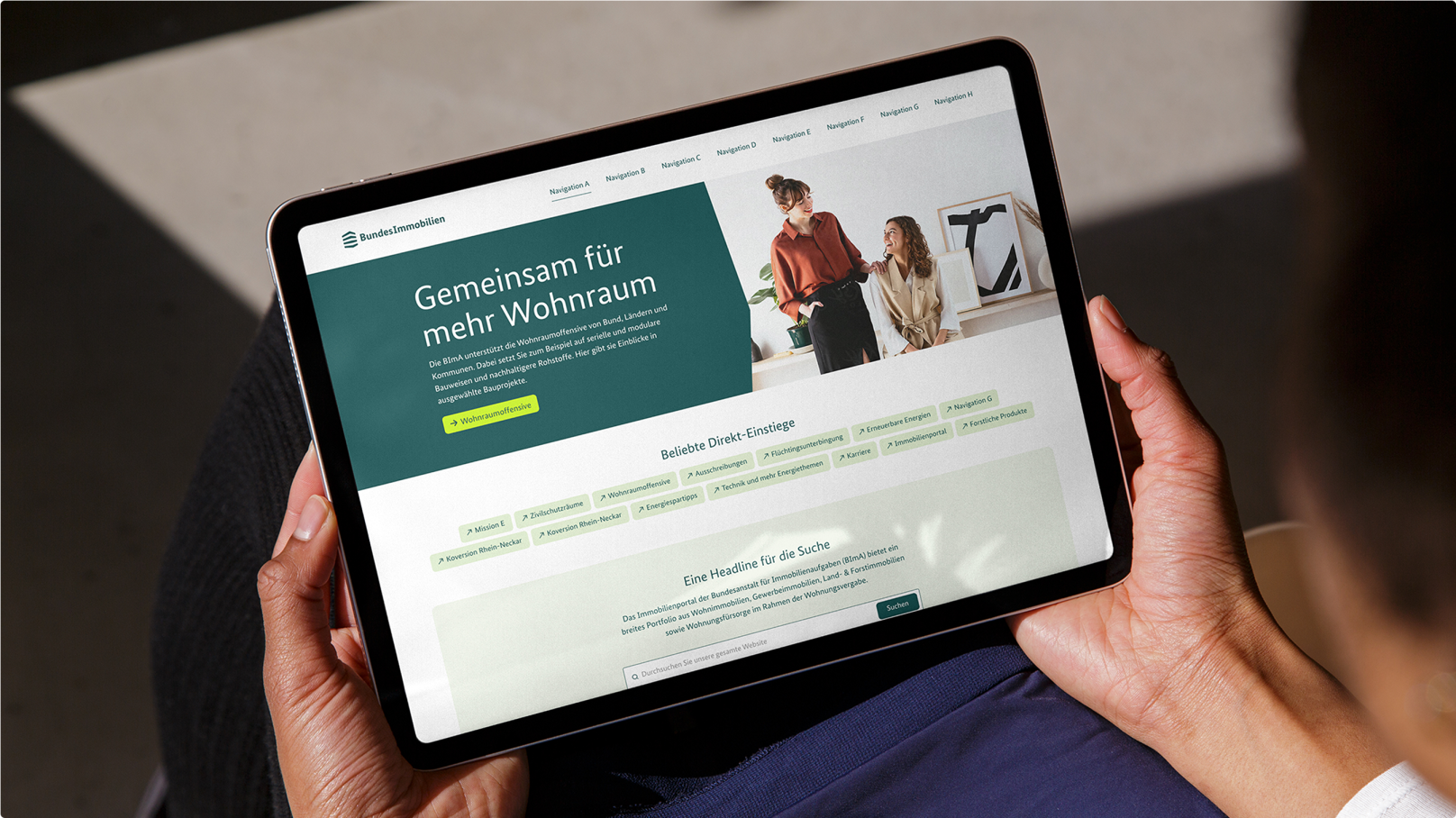 Eine Person hält ein Tablet, das die Website der Bundesimmobilien mit einem Titel, einem Bildund mehreren Navigationsoptionen zeigt.